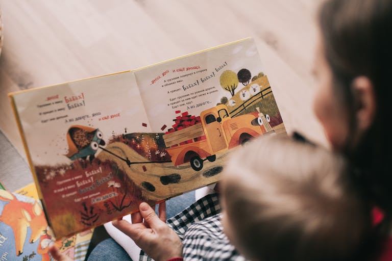 A mother and toddler sharing a story from an illustrated children's book indoors.