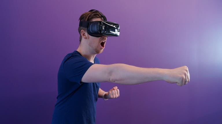 Caucasian man immersed in virtual reality using VR headset, making a punching gesture against a purple backdrop.