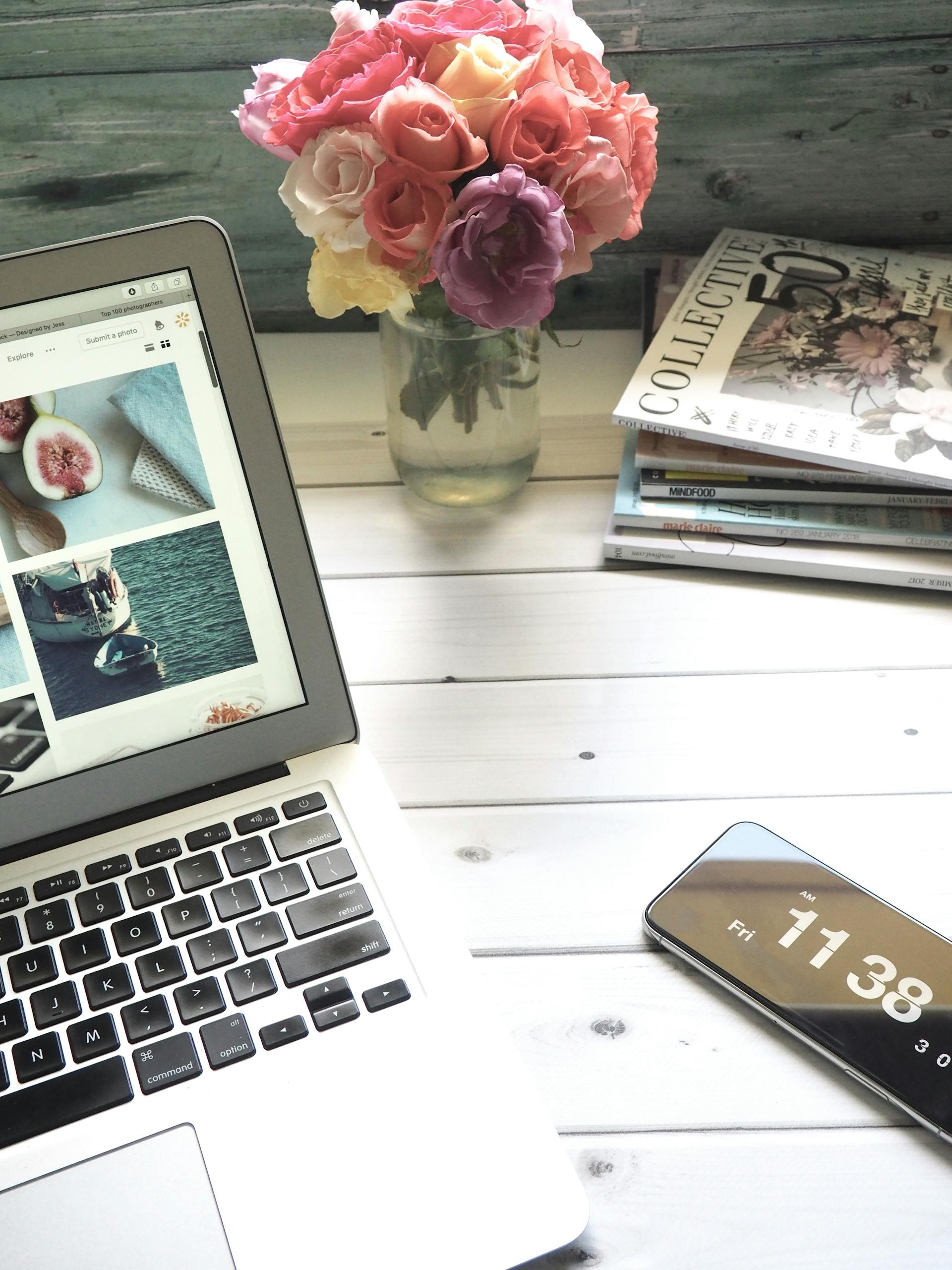 Elegant workspace featuring a laptop, smartphone, and fresh roses in a bright setting.