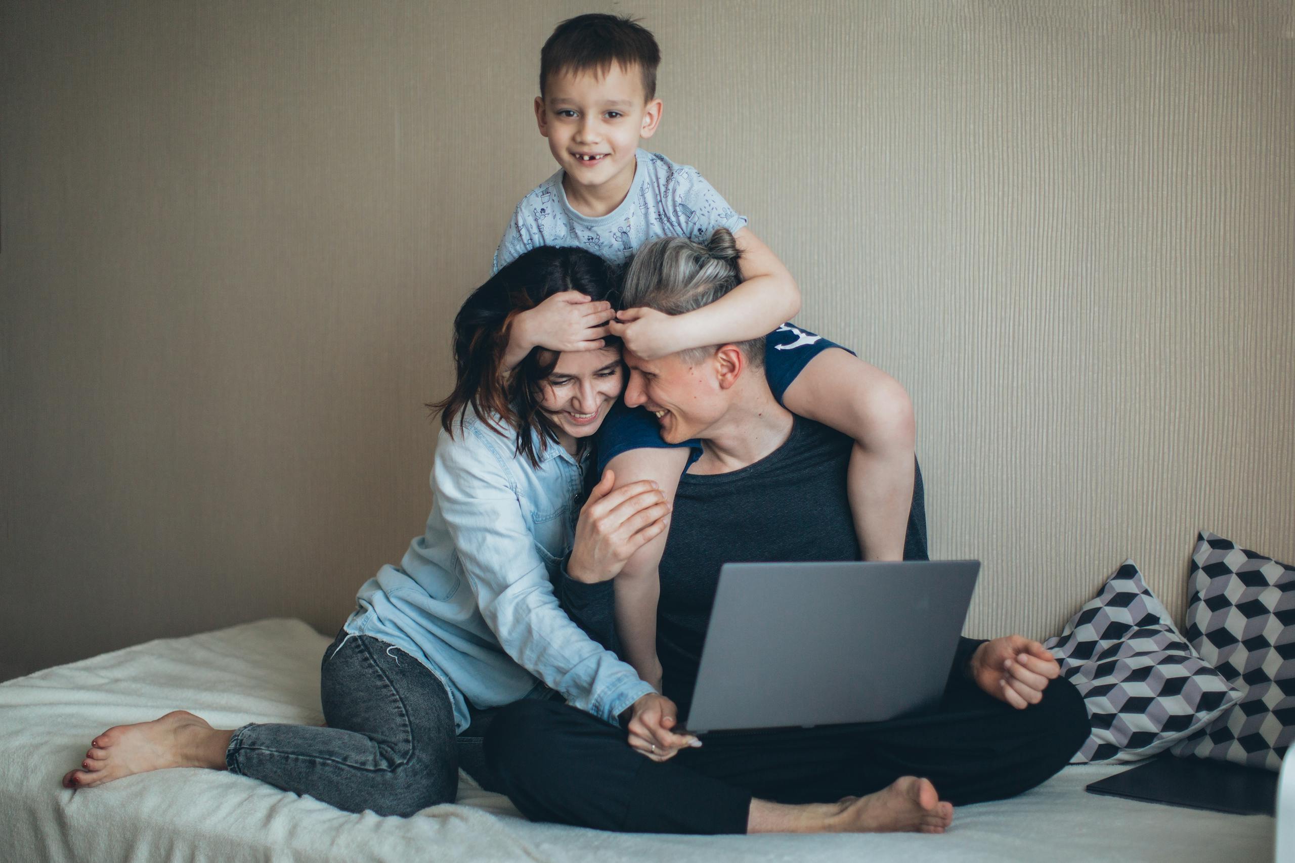 Family enjoying time together on bed, using a laptop. Remote work and bonding combined.