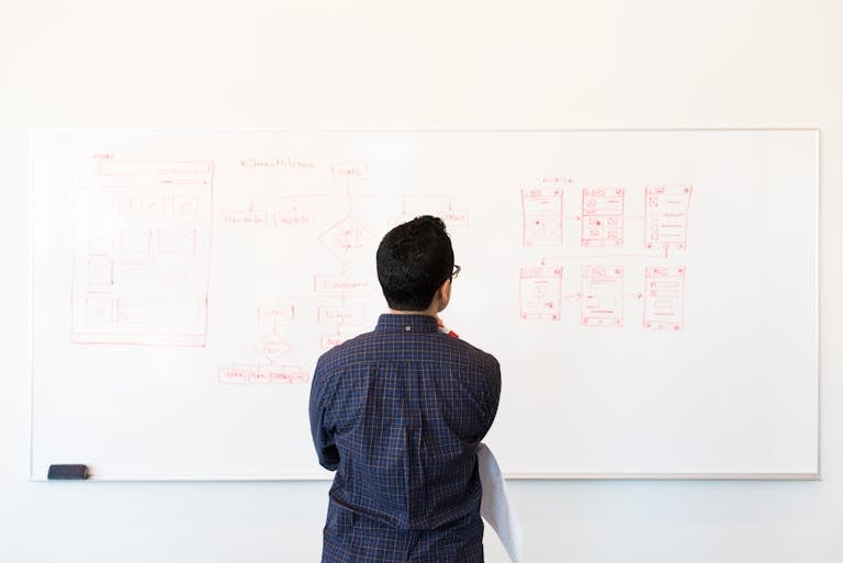 Man standing at a whiteboard planning UX design concepts in a modern office setting.